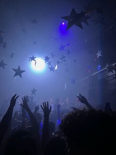 many people are reaching for stars in the air at a concert with blue and white lights