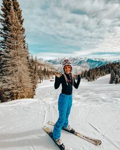 a woman standing on skis in the snow with mountains in the backgroud