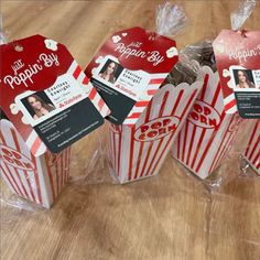 three red and white striped popcorn boxes with labels on them sitting on a wooden table