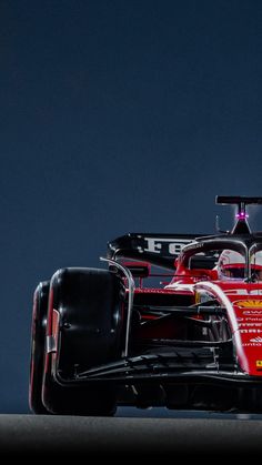 a red race car driving on a track with dark sky in the backround