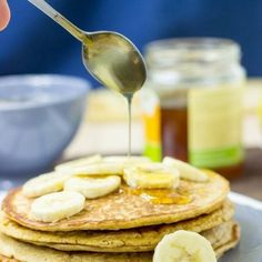 a person pouring syrup on top of pancakes with bananas and honey in the background,