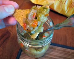 a person holding a spoon full of food in a glass jar with chips on the side