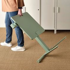 a person standing next to a green table on top of carpeted floor in front of white cupboards