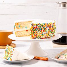 a cake with white frosting and sprinkles sits on a plate next to other cakes