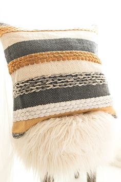 a pillow that is sitting on top of a stool next to a white chair with a black and tan striped pillow