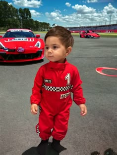 a little boy in a race suit standing next to a red sports car on the track