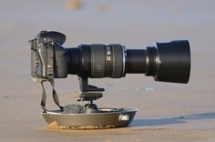 a camera sitting on top of a metal bowl in the sand at the beach with it's lens attached