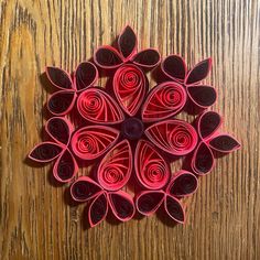 an origami flower made out of red paper on a wooden surface with leaves