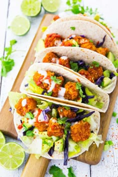 three chicken tacos on a cutting board with lime wedges and cilantro