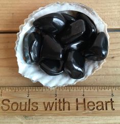 a bowl filled with black stones sitting on top of a wooden table next to a ruler