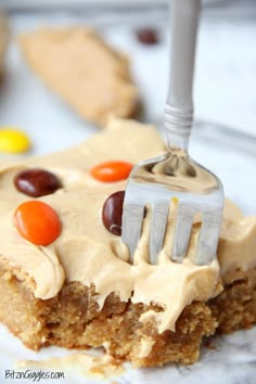 a piece of cake with frosting and candy on top is being held by a fork