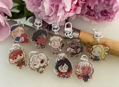 six keychains with cartoon characters on them sitting next to pink carnations