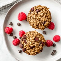 two oatmeal cookies with raspberries on a white plate next to chocolate chips