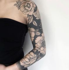 a woman wearing a black dress with flowers on her arm and arms, in front of a white wall