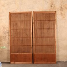 two brown wooden doors sitting next to each other on a cement ground near a wall