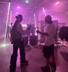 two men in white shirts and black shorts are talking to each other with purple lights behind them