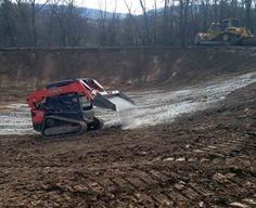 a tractor is driving through the mud in front of a bulldozer on a dirt road