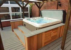 a hot tub sitting on top of a wooden floor next to a brick building with windows