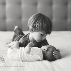 a little boy laying on top of a bed next to a small baby holding it's head