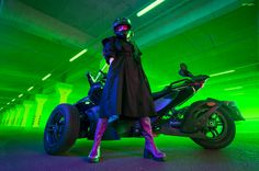 a woman standing next to a motorcycle in a parking garage with neon green lighting on the walls