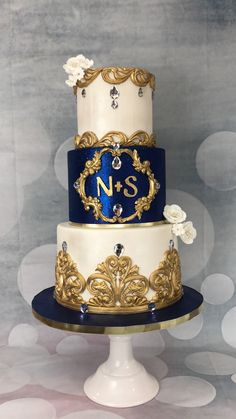 a three tiered cake with blue and gold decorations on top, sitting on a pedestal