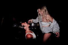 two women in the dark one is cutting another woman's hair and she is wearing a white top