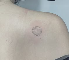 the back of a woman's shoulder with a small shell tattoo on her left shoulder