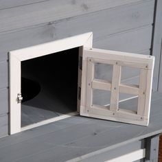 an open window sitting on top of a wooden shelf next to a gray house wall