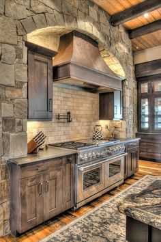 a kitchen with an oven, stove and counter top in stone walled wall above hardwood flooring