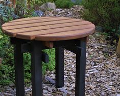 a wooden table sitting on top of a pile of leaves next to a garden area