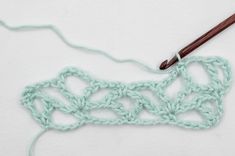 the crochet pattern is being worked on with a wooden knitting needle and yarn