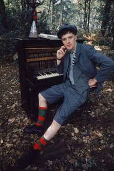 a man sitting on a bench next to a piano in the woods with his feet up