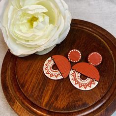 two wooden earrings sitting on top of a wooden tray next to a white flower in a vase