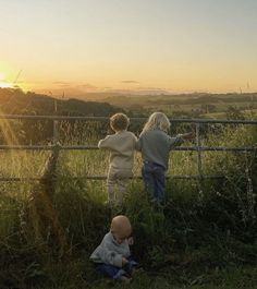 two children looking over a fence at the sunset