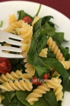 a white plate topped with pasta and spinach salad next to a fork on top of it