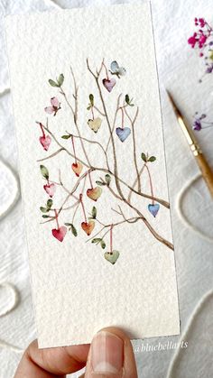 a hand holding up a card with watercolor hearts on it and a pen next to it