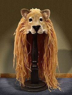 a lion head with long hair on top of a black pole in front of a wall