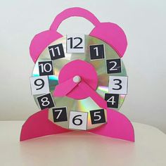 a pink clock sitting on top of a table next to a white wall with numbers