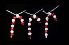 three necklaces with red and white beads hanging from chains on a black background,