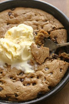 a chocolate chip cookie with ice cream in a black bowl on a wooden table top