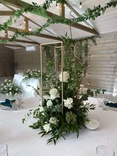 white flowers and greenery on a table in a room with wooden beams, glassware and candlesticks