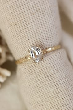 a diamond ring sitting on top of a white cloth next to a pine tree branch