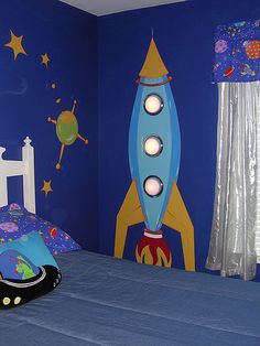 a child's bedroom with a rocket ship painted on the wall and blue bedding