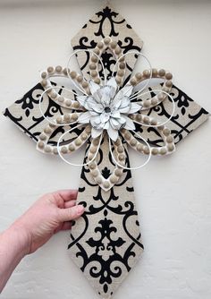 a hand is holding up a decorative cross made out of fabric and buttons on the wall