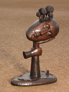 a bronze sculpture of a woman's head with three birds on her head, in the middle of a dirt area