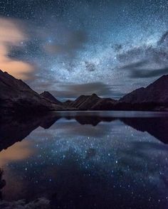 the night sky is filled with stars and clouds over a body of water in front of mountains