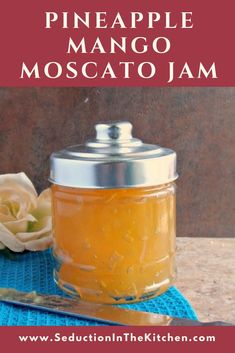 a jar of pineapple mango moscato jam on a blue towel next to a spoon