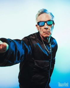 an older man wearing sunglasses and pointing his finger at the camera while standing in front of a blue background