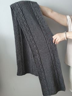 a woman is holding up a gray knitted blanket