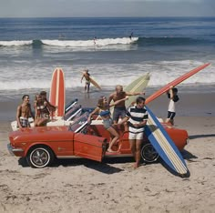 a group of people standing on the beach with surfboards and a car in front of them